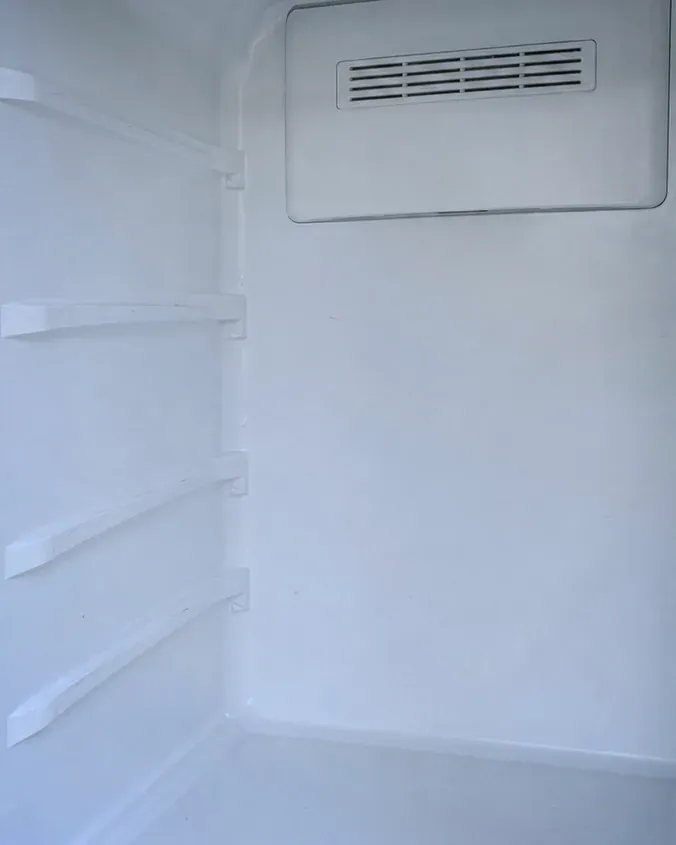 Tall, empty white refrigerator compartment with a vent cover at the top of the back wall.