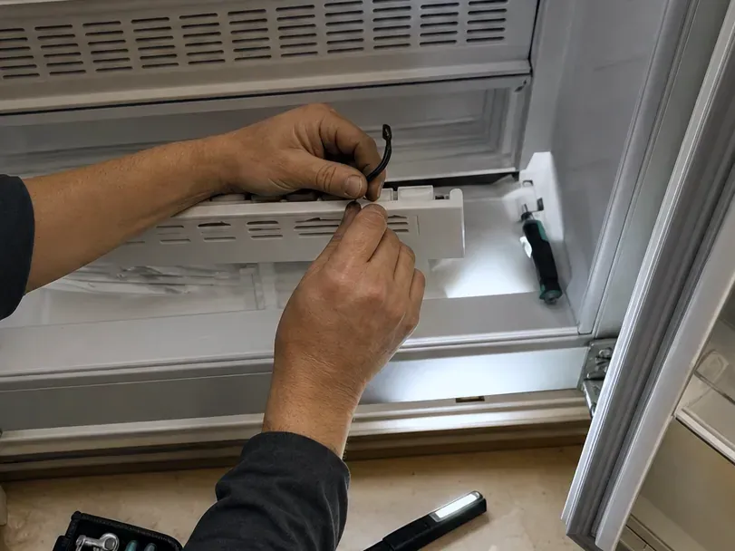 Two hands working on a part at the back of a lit lower compartment, a flashlight on the floor in front.